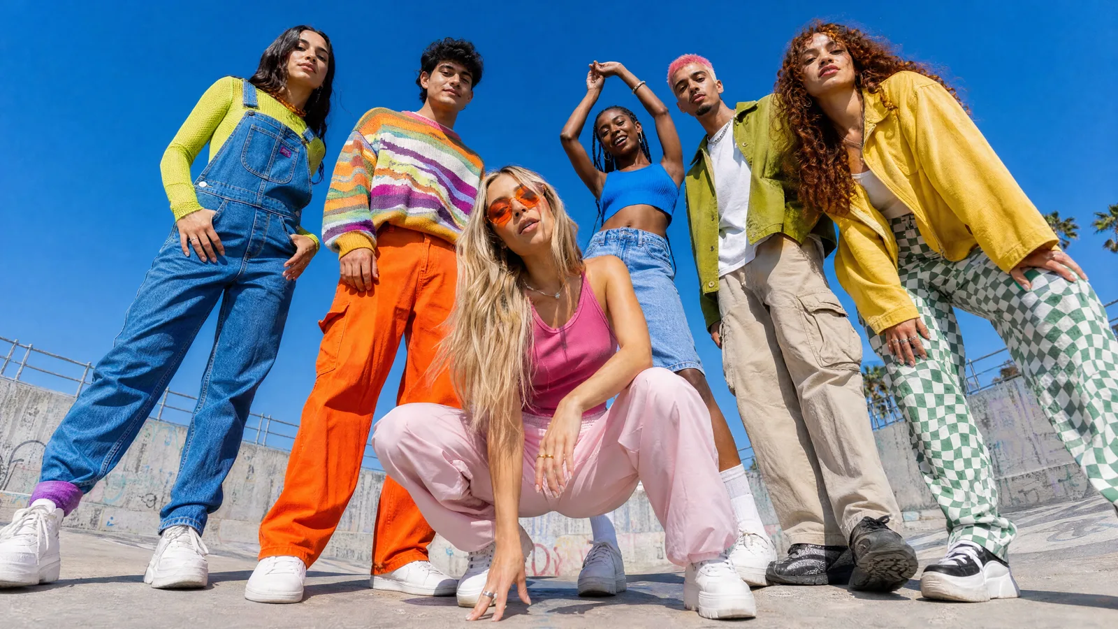 Six friends in bright colors posing together against a white wall, grinning at the camera.